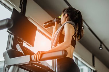 Koşu bandında su içen genç bir kadın. Koşu bandında protein içen genç bir kadın..