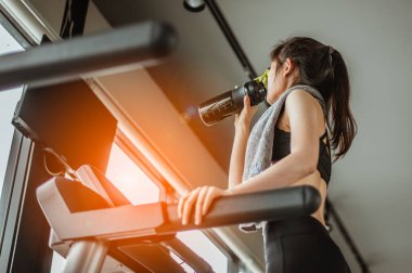 Koşu bandında su içen genç bir kadın. Koşu bandında protein içen genç bir kadın..