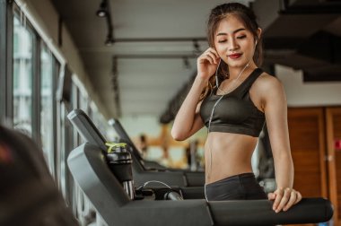 Spor salonunda koşu bandında koşan kadın portresi müzik dinliyor.Egzersiz konsepti. Fitness ve sağlıklı yaşam tarzı..