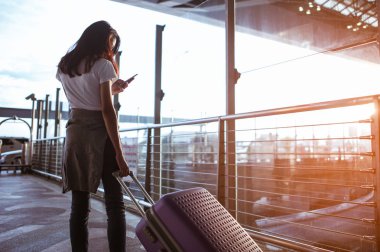 Modern havaalanı terminalinde bavulu çeken genç bir kadın. Taşıyıcıyı beklerken bavuluyla gezen adam. Dikiz aynası. Boşluğu kopyala