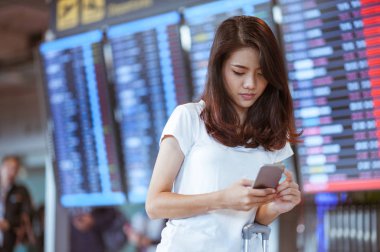 Uluslararası havaalanında uçuş bilgi panosunun yanındaki cep telefonunu kullanan bir kadın., 