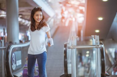 Modern havaalanı terminalinde bavulu çeken genç bir kadın. Taşıyıcıyı beklerken bavuluyla gezen adam. Dikiz aynası. Boşluğu kopyala