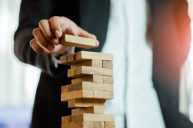 İşadamı elini kaldırıyor ya da modern ofisteki kuleye tahta bloğu yerleştiriyor. Plan ve iş stratejisi. Arkaplan için bulanık.