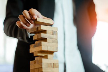 İşadamı elini kaldırıyor ya da modern ofisteki kuleye tahta bloğu yerleştiriyor. Plan ve iş stratejisi. Arkaplan için bulanık.