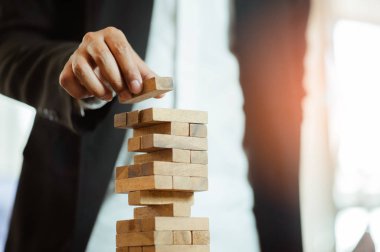 İşadamı elini kaldırıyor ya da modern ofisteki kuleye tahta bloğu yerleştiriyor. Plan ve iş stratejisi. Arkaplan için bulanık.