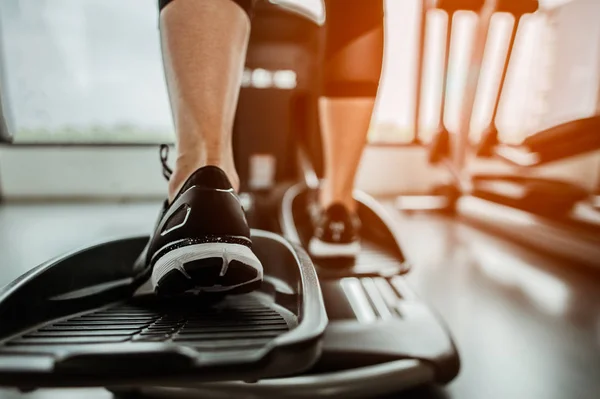 Bir eliptik üzerinde kardiyo çalışmasının yakın bacağı. İnsanlar spor salonunda eliptik bir antrenörle çalışıyor. 