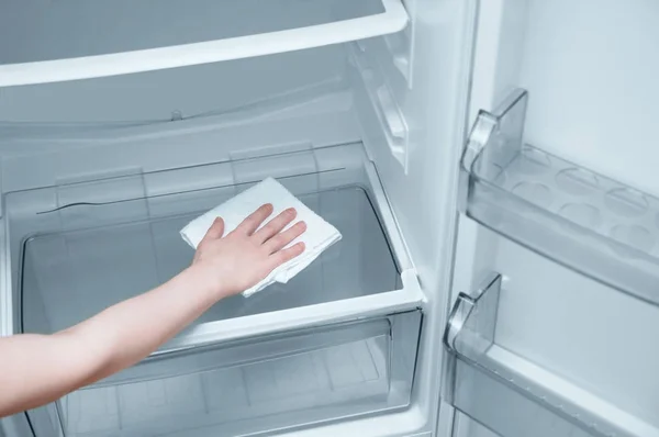 The girl's hand with a white rag washes the refrigerator