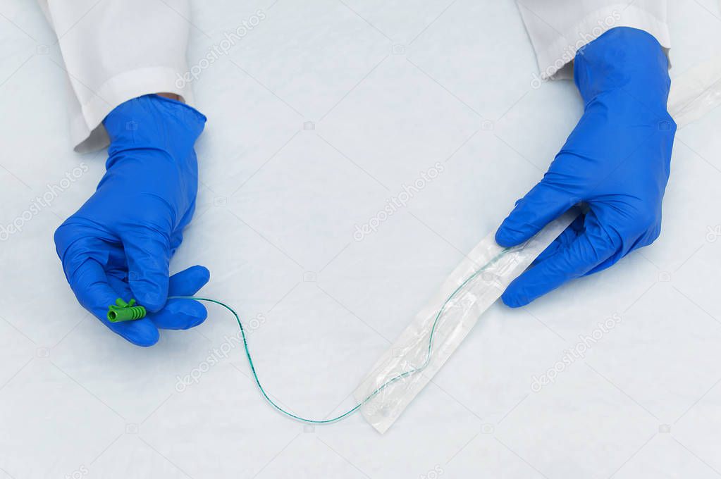 The hands of a urologist in a white lab coat and blue sterile gloves take out a catheter from a sterile package
