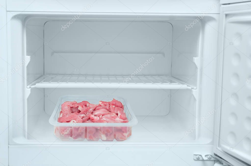 Tray with fresh chopped meat inside a white freezer.Close-up