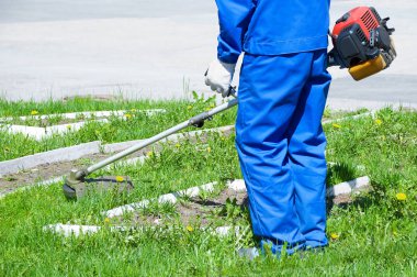 Bir erkekte mavi iş yarı tulumlar çim çim biçme makinesi ile mows. Yakın çekim