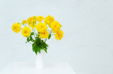 Bir buket sarı çiçek Heliopsis beyaz bir vazo içinde. Bir odada beyaz şifonyerin üzerinde.
