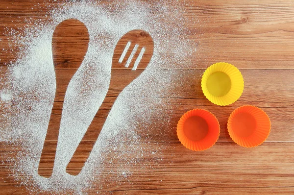Spilled flour on the table. Spoon-shaped imprint in flour and cake molds. Wooden brown background.