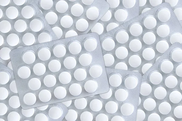 White round pills in packs are scattered on the surface. Close-up.