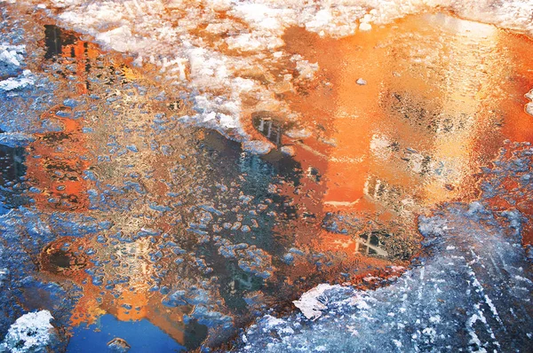 Reflection of a house in an ice puddle in spring. Melting snow.