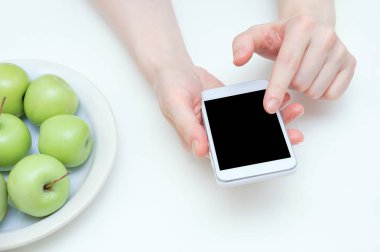 Diyet kavramı. Beyaz bir kızın elinde bir akıllı telefon ve masada bir tabak elma. Close.