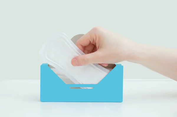 Beyaz kız kutudan kadın günlük sıhhi pedleri çeker. Gri arka plan.