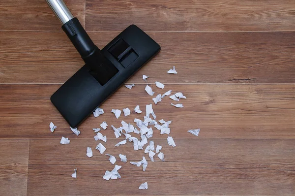 House cleaning. Collecting paper trash vacuum cleaner on wooden brown floor.