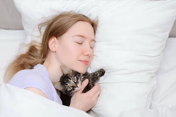 Caucasian girl with a small kitten sleeping on a white pillow in bed. View from above.