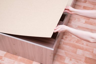 Assembling furniture. The Caucasian girl holds wooden flooring for the slatted bottom of the bed. clipart