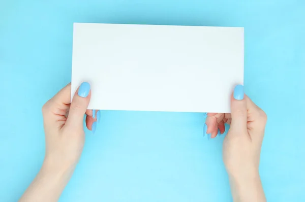 White sheet of paper in the hands of a caucasian girl. Manicure on the nails. Turquoise background.