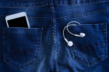 Beyaz akıllı telefon ve kulaklıklar mavi kot yakın çekim bir cebinde.