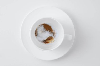 Pudra kahve tozu ve susuz şeker ve beyaz arka planda bir fincan çay tabağı..