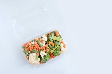 Beyaz arka planda şeffaf plastik bir kabın içinde donmuş sebze karışımı..