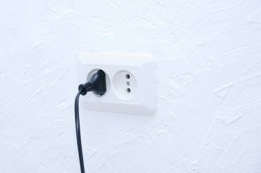Elektrikli bir aletin siyah fişi beyaz bir elektrik prizine takılmış..