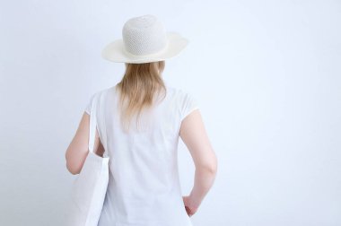 Sıfır atık. Sırtı kameraya dönük beyaz tişörtlü, omuzunda pamuk bir çantayla beyaz bir kadın..