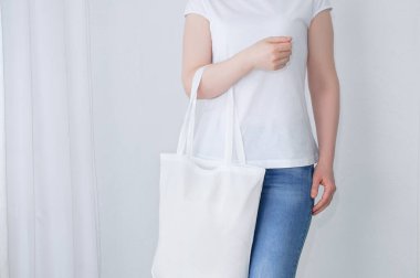 Sıfır atık. Elinde pamuk bir çantayla beyaz tişörtlü beyaz bir kadın..