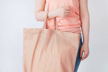 Sıfır atık. Elinde pamuk bej bir çantayla mercan bluzlu beyaz bir kadın..