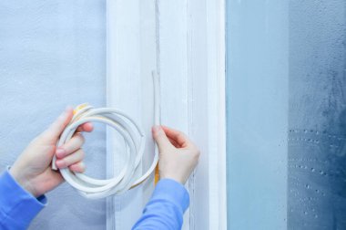 Caucasian woman glues window rubber insulation to the window frame close-up. clipart
