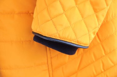 Sarı ceketli siyah manşetli bir kolun yakın çekimi..