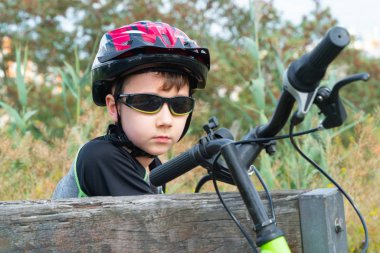 Koruyucu kasklı okul çocuğu Park'ta bisikletli bir bankta oturuyor..
