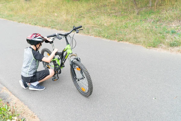Ragazzo della scuola nel casco protettivo fissare bici sulla strada . — Foto Stock