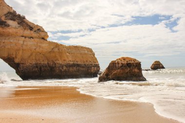 Kayalıklarla plaj ile parlak ve bulutlu gökyüzü (Algarve, Portekiz)
