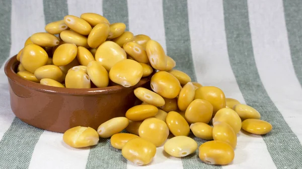 Earthenware bowl full to the brim with salted lupin beans, on top of a stripped gray cloth towel. — Stock Photo, Image