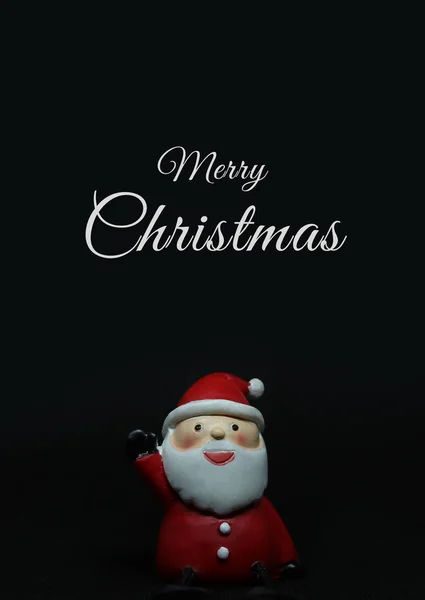 Adorable muñeca santa claus sobre fondo negro con texto blanco de Feliz Navidad arriba . — Foto de Stock