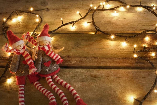 Par de adorables y lindos elfos de Navidad sentados en una mesa de madera rústica con luces amarillas de Navidad. Con espacio de copia . — Foto de Stock