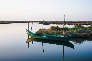 Aydınlık bir günde huzurlu ve güzel bir lagün lekile kıyıya yakın yıpranmış küçük bir tekne. Su üzerinde tekne yansıması.