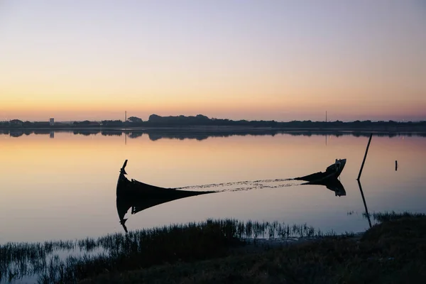 Bir gün batımında, Aveiro Lagünü kıyısına yakın bozulmuş ve batık tekne. Su yansımaları ile.