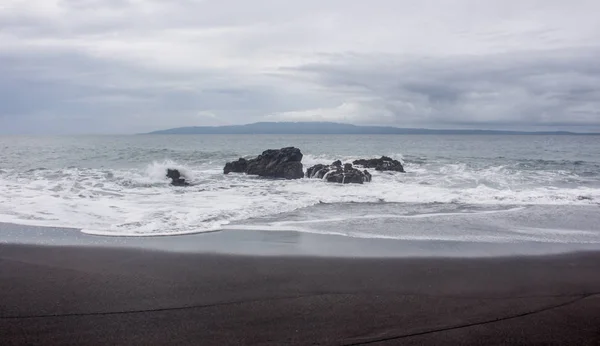 Ondas batendo na praia de areia preta vazia em Bali com a ilha Nusa Penida à distância. Pantai Wates, Indonésia — Fotografia de Stock