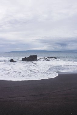 Beyaz köpük dalgalar yavaşça kayalar ve siyah kum içine çökmesini. Bali, Endonezya güneyinde Pantai Wates plaj Kıyıları.