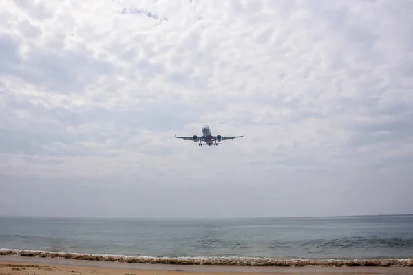 Plane over Nai Yang beach almost landing in Phuket airport during a cloudy day, with small waves crashing into sand Royalty Free Stock Photos