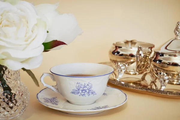 Buquê de rosas, uma xícara de porcelana de porcelana fina e um chá de prata definido em um fundo amarelo. Conceito para chá da tarde — Fotografia de Stock
