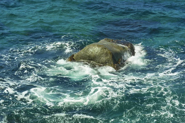 Stone in the sea, around white foam. Sea water and stone. Underwater stone, sea foam around the stone, water movement