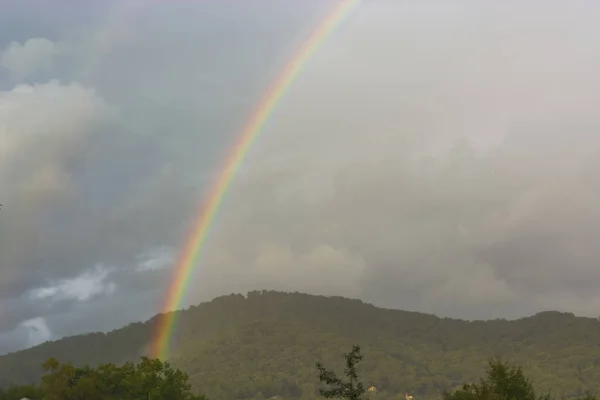 天空中有一道明亮的彩虹 在遥远的青山 一条明亮的彩虹 衬托着天空和青山的背景 天气的变化 雨后的雷雨 图库图片