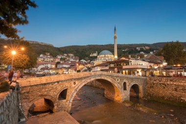 Kosova 'nın Prizren kentindeki eski taş köprü ve eski Osmanlı Sinan Paşa Camii' nin gece manzarası. Bistrica nehrinin kıyısında yer alan tarihi şehir güneş battıktan sonra gökyüzü ile güzel bir gece manzarası.