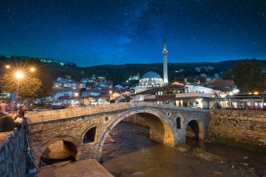 Kosova 'nın Prizren kentindeki eski taş köprü ve eski Osmanlı Sinan Paşa Camii' nin gece manzarası. Bistrica nehrinin kıyısında yer alan tarihi şehir güneş battıktan sonra gökyüzü ile güzel bir gece manzarası.