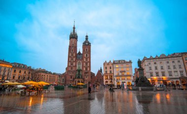 KRAKOW - POLAND - 01 Nisan 2019: St Mary Bazilikası (Mariacki Kilisesi) ve beyaz vagonlar Eski Krakow Kasabası 'ndaki Ana Pazar Meydanı' nda gece aydınlatıldı (Krakow))